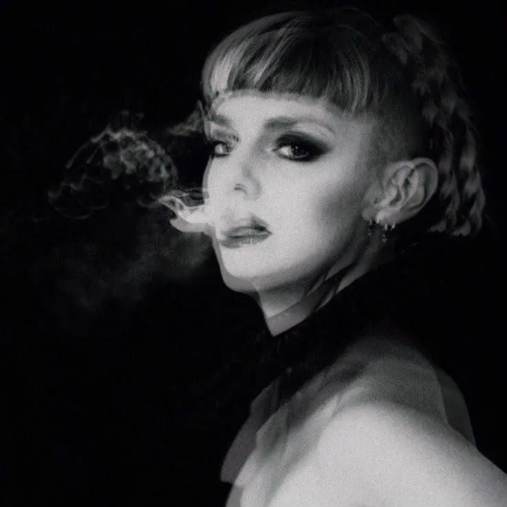 Oli Gosh in black and white, turning to the camera with smoke drifting from her mouth.