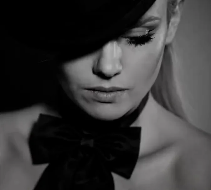Oli Gosh in black and white, under a black hat, a large bow at her neck